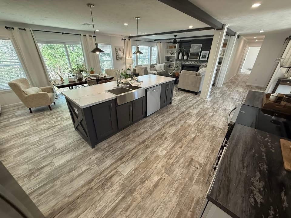 Modern open-concept kitchen and living room with wood-like flooring, dark kitchen island, dining table, and cozy seating area by a fireplace.