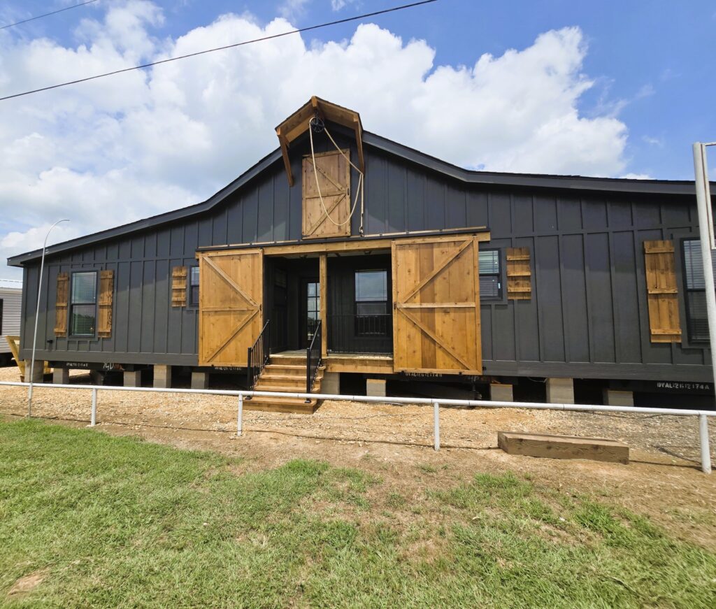 Large, dark gray barn-style building with wooden shutters and double doors. Elevated on piers, it sits under a partly cloudy sky, conveying rustic charm.