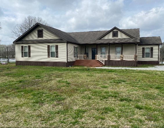 A beige ranch-style house with brown shutters, a front porch, and steps leading up to it. The foreground is a grassy yard under a cloudy sky.
