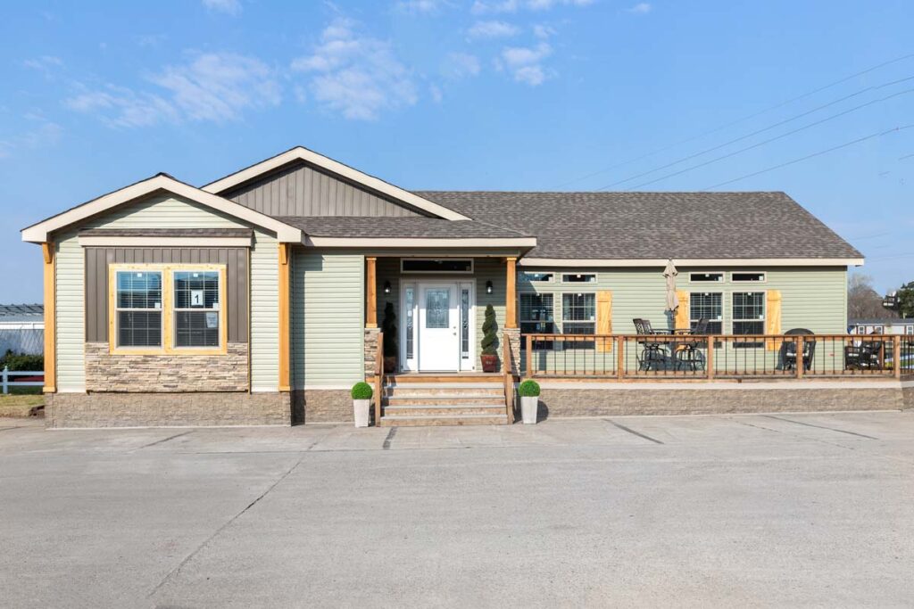 Single-story house with beige siding and stone accents. Front porch with chairs, potted plants, white double doors, under a clear blue sky.