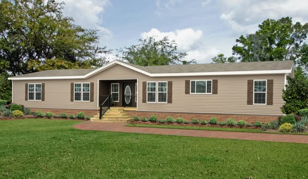 A beige, single-story house with white trim and brown shutters sits amidst a well-manicured lawn. A brick path leads to the front door, flanked by bushes. Sky is partly cloudy.