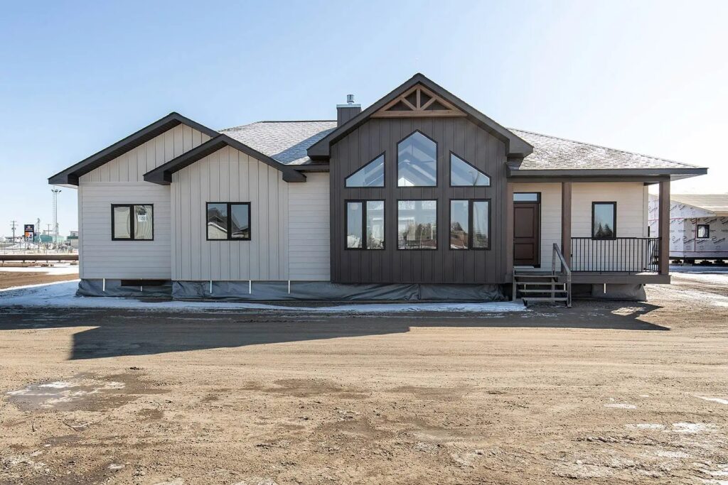 Modern one-story house with large windows and a triangular roof detail, set on a dirt lot with a clear blue sky, conveying a serene suburban vibe.