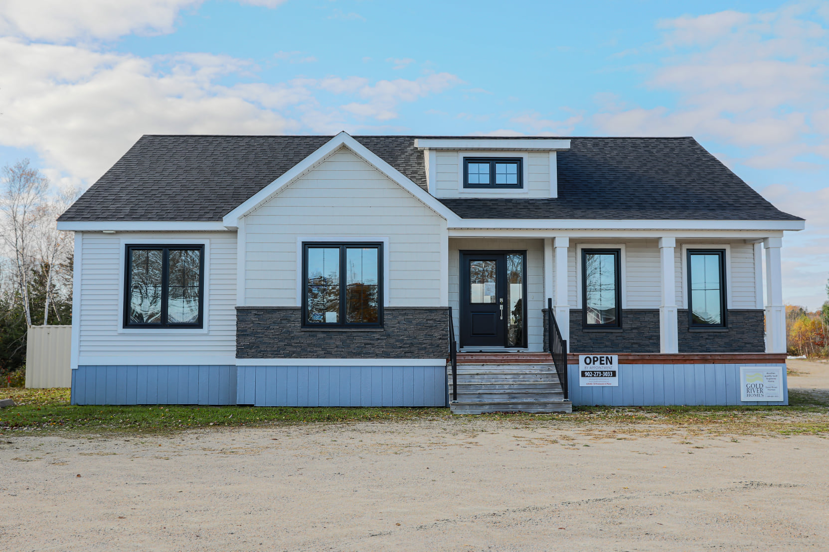 Single-story house with white siding and dark stone accents under a clear blue sky. A sign reads "Open." The setting is calm and inviting.