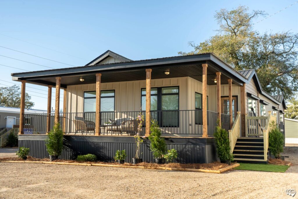 Modern modular home with a spacious wraparound porch, wooden columns, and potted plants. Warm lighting and natural tones create a welcoming atmosphere.