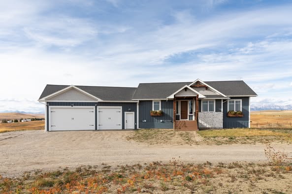 Single-story blue house with a dark roof and attached white garage, set on a barren landscape under a partly cloudy sky, conveying solitude.