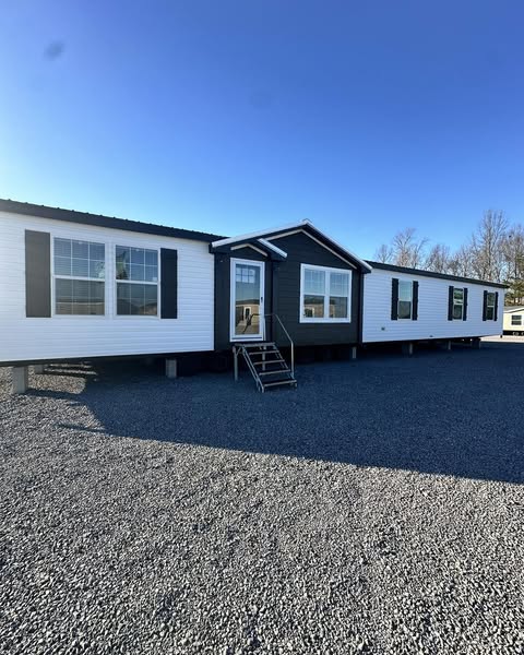 A modern white and black mobile home with large windows sits on a gravel lot under a clear blue sky, conveying a bright and welcoming atmosphere.