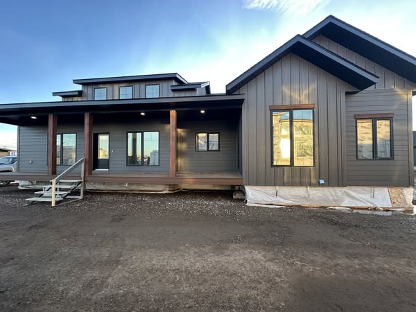 A modern, single-story house with a large wooden porch, dark siding, and tall windows. The sky is clear, creating a calm and inviting tone.
