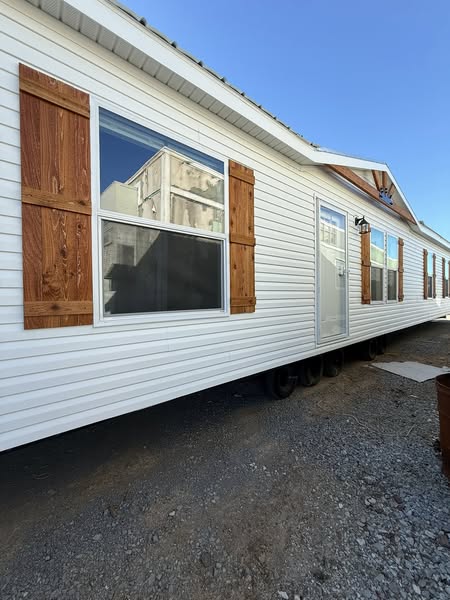 White mobile home with brown wooden shutters lined up on a gravel lot under a clear blue sky, exuding a sense of simplicity and readiness.