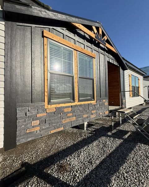 Single-story modern house exterior with gray and brick-textured facade, large windows, wooden trim, and a small staircase under clear blue sky.