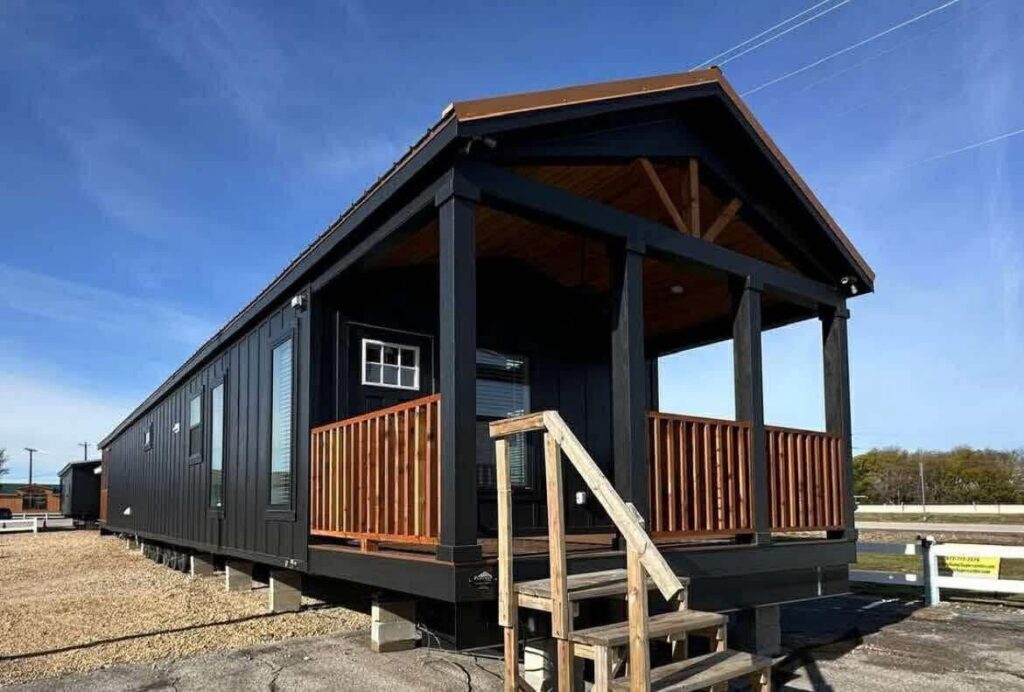 Modern tiny house with black siding and brown accents, featuring a small front porch and steps, set under a clear blue sky in a sunny area.