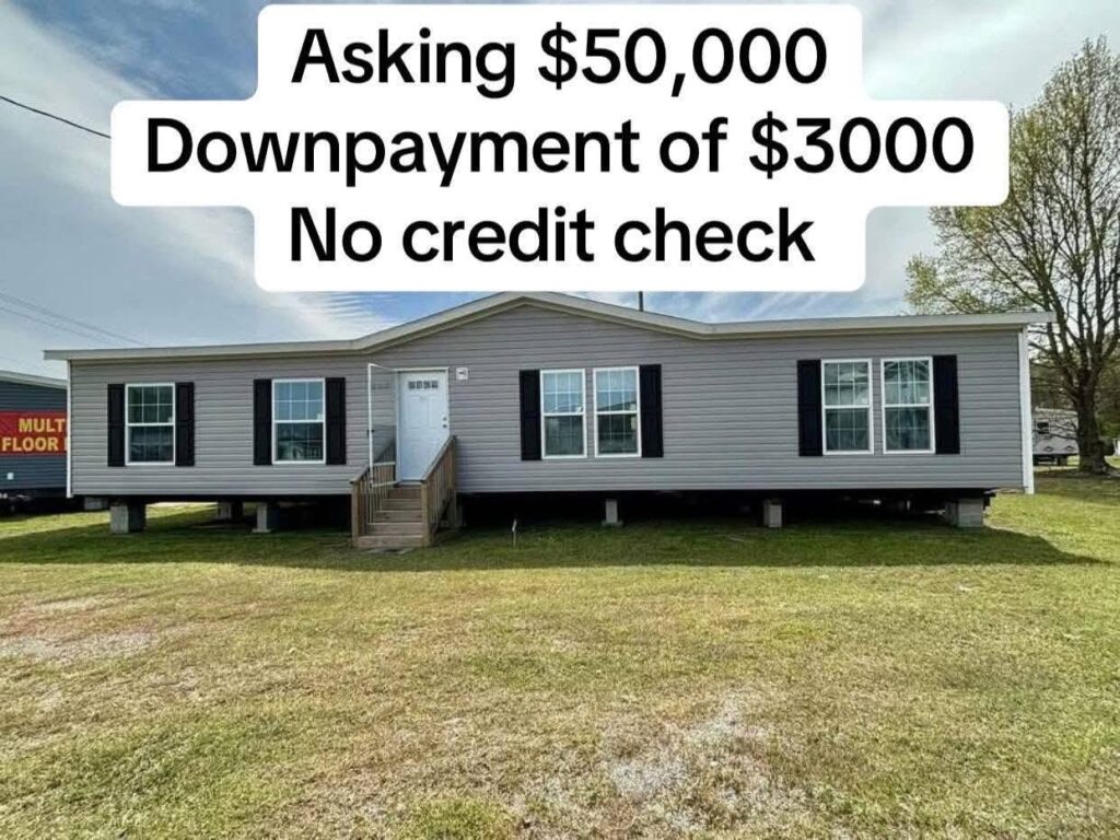 Image of a gray mobile home with white trim set against a grassy yard under a partly cloudy sky. Text above reads: "Asking $50,000. Downpayment of $3000. No credit check."