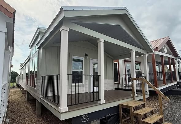 A row of quaint, elevated tiny houses with front porches, wooden stairs, and railings. The scene conveys a peaceful, inviting atmosphere under a cloudy sky.
