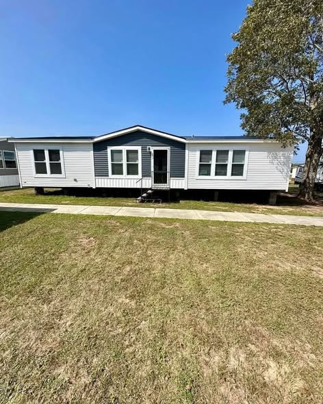 A white and blue single-story manufactured home with a front porch, set on a manicured lawn under a clear blue sky, creating a serene atmosphere.