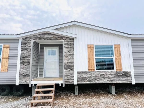 Single-story modular home with stone accents, wooden shutters, and a small porch with steps. The facade conveys a modern and welcoming feel.