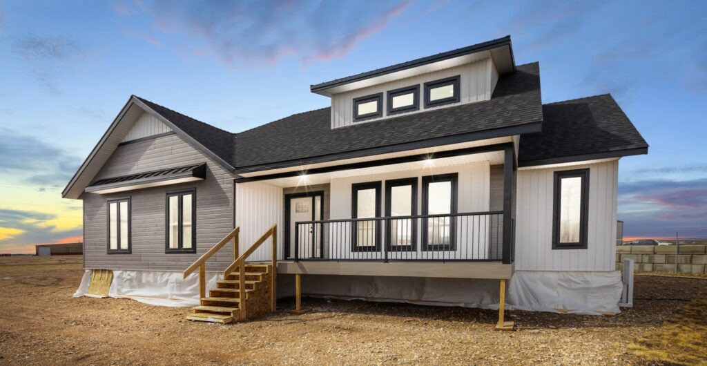 Modern single-story house with dark gray siding and white trim, a front porch with steps, set against a serene sunset sky on a dry, open landscape.