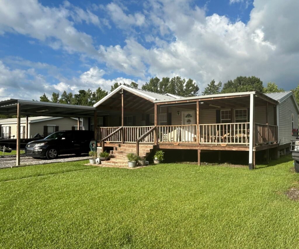 House with a wooden porch and green lawn under a partly cloudy sky. A black van is parked on a gravel driveway, creating a calm suburban scene.