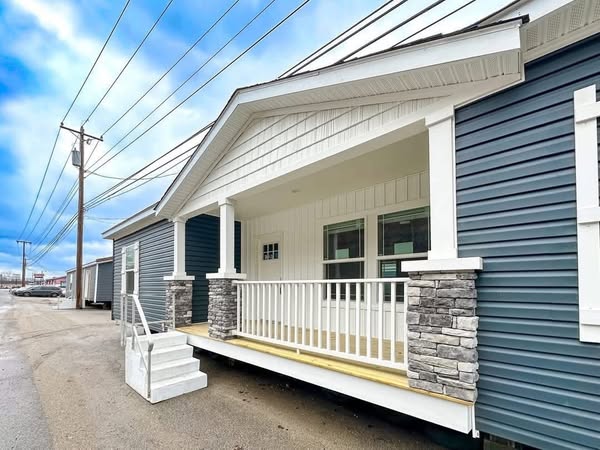 A modern house with blue siding and white trim. Features a stone-accented porch, white railings, small entry stairs, under a bright blue sky.