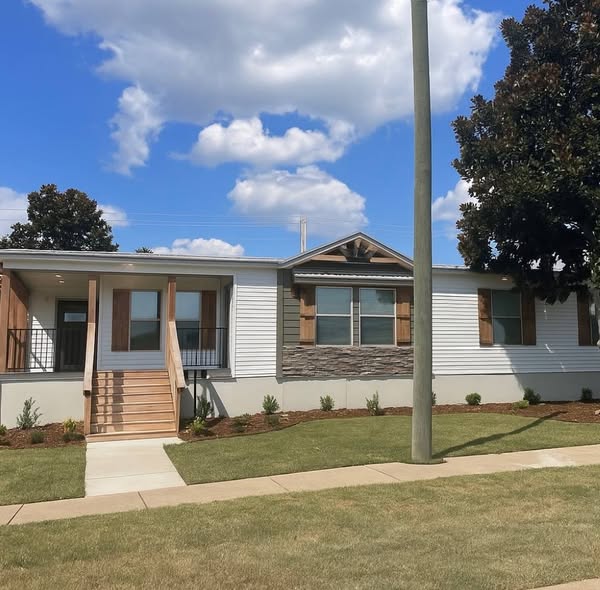 A modern white house with stone accents, wooden shutters, and a front porch. It's set against a clear blue sky with fluffy clouds, conveying tranquility.