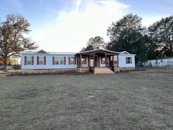 A single-story white house with a covered porch is centered in a large grassy yard. Mature trees surround the home, creating a serene atmosphere.
