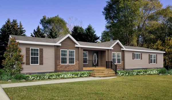 A single-story, brown modular home with white trim and a pitched roof, surrounded by green grass and trees, exuding a serene, welcoming vibe.