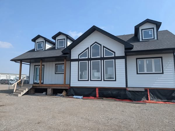 A modern, two-story house with a white and black exterior, featuring large triangular and rectangular windows. The gravel foreground and blue sky add a serene tone.