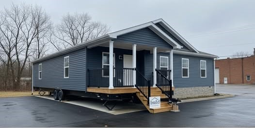 Exterior and interior view of a modern modular home. The outside features dark gray siding and a small porch. Inside, there's a cozy living area with neutral sofas, a wooden coffee table, a kitchen with wooden cabinets, pendant lights, and a built-in storage bench. The space feels inviting and contemporary.