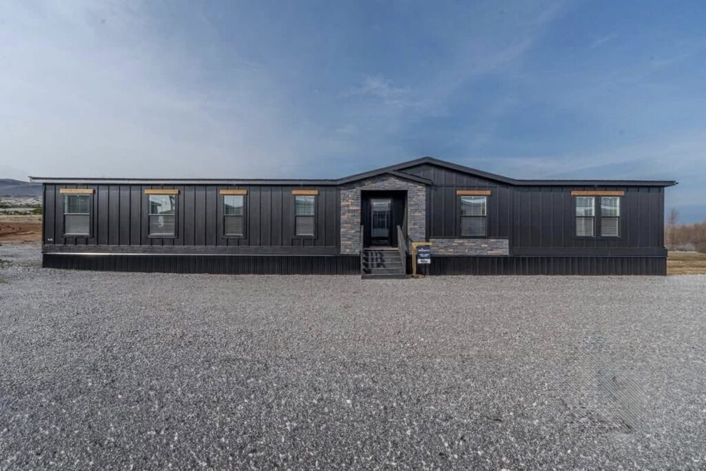 Wide, modern black building with four windows and a central entrance, set against a gravel foreground and a clear blue sky, conveying a sleek, contemporary feel.