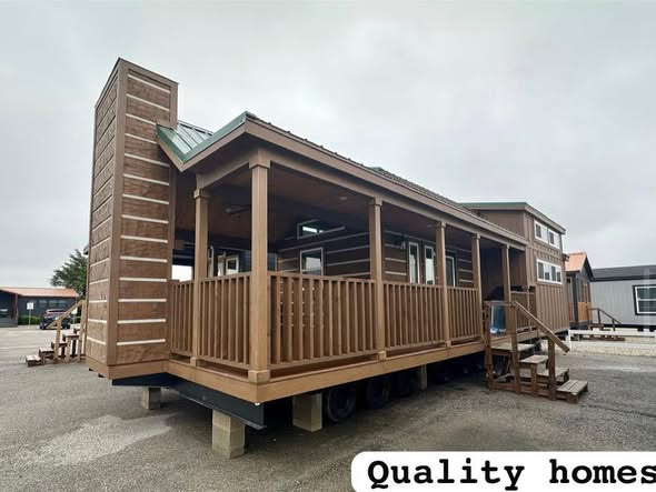A modern tiny house on a lot, featuring a raised wooden porch and large windows, set under a cloudy sky, with "Quality homes" text in the corner.