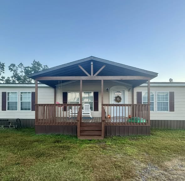 Front view of a beige manufactured home with a welcoming wooden porch. Lawn chairs are placed on the porch, and a wreath decorates the door, creating a cozy atmosphere.