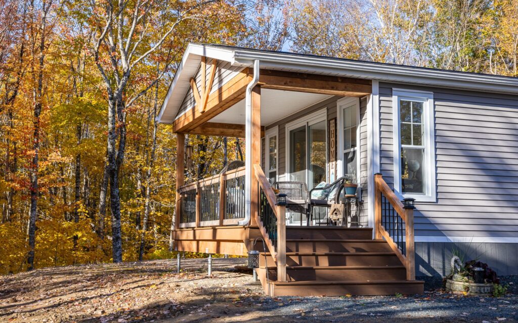 Cozy cabin with a wooden porch, surrounded by autumn trees with vibrant yellow leaves. The warm sunlight casts soft shadows, creating a serene atmosphere.
