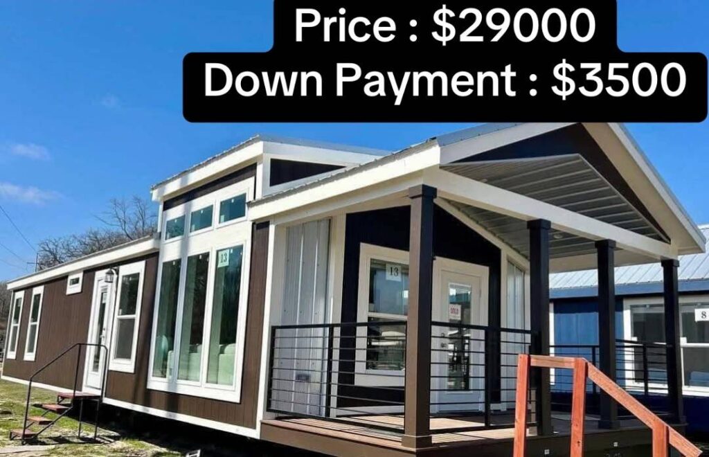 A brown and white manufactured home with large windows and a covered porch. The sky is clear blue. Text overlay shows price: $29,000 and down payment: $3,500.