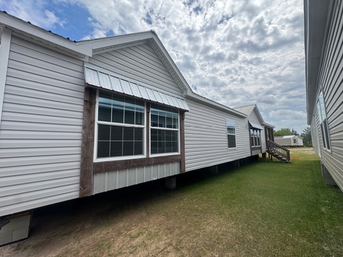 Single-story manufactured home with white siding and large windows under a cloudy sky. It's set on grassy land, exuding a calm, rural vibe.