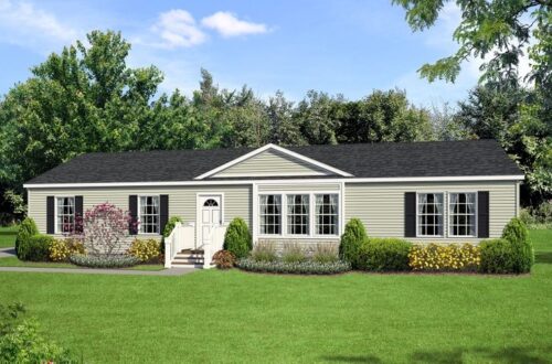 A single-story, beige modular home with black shutters, surrounded by lush greenery and flowering shrubs, under a clear blue sky. Calm and inviting tone.