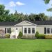 A single-story, beige modular home with black shutters, surrounded by lush greenery and flowering shrubs, under a clear blue sky. Calm and inviting tone.