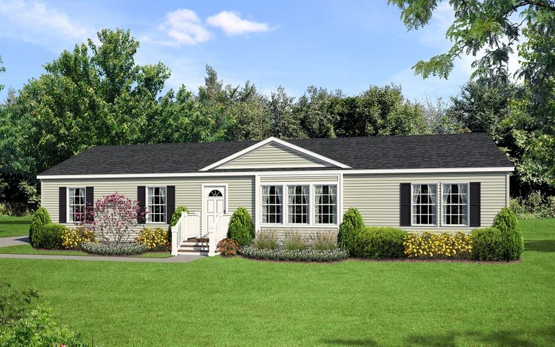 A single-story, beige modular home with black shutters, surrounded by lush greenery and flowering shrubs, under a clear blue sky. Calm and inviting tone.