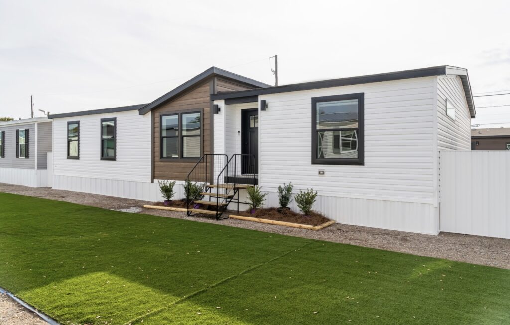 Modern white mobile home with a dark brown accent and black-framed windows, set on a neat green lawn, conveying a clean and welcoming atmosphere.