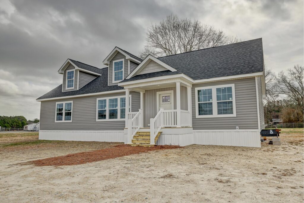 A newly constructed, single-story gray house with white trim and a black roof sits on a bare lot under a cloudy sky, conveying a fresh start.