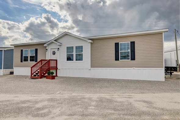 Single-story modular home with beige siding, white trim, and red steps leading to the entrance. Overcast sky in the background conveys a calm mood.