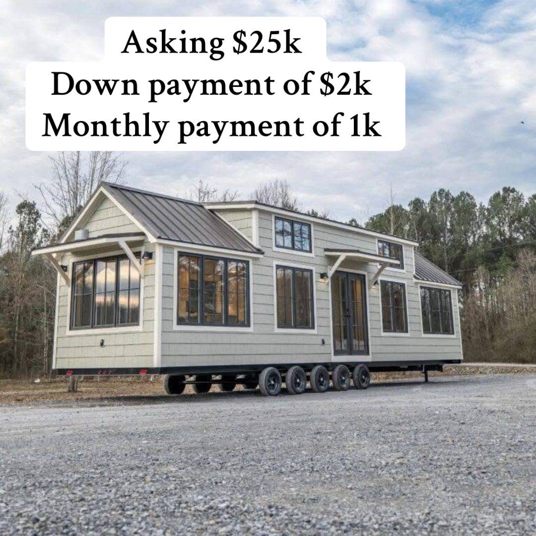 Tiny house on wheels with gray siding and multiple windows, situated on a gravel lot. Text above details sale price and payment terms. Cloudy sky behind.