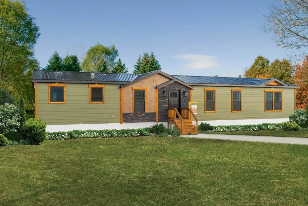 Single-story manufactured home with light green siding, a black roof, and wood accents. Surrounded by lush trees and a manicured lawn under a clear sky.