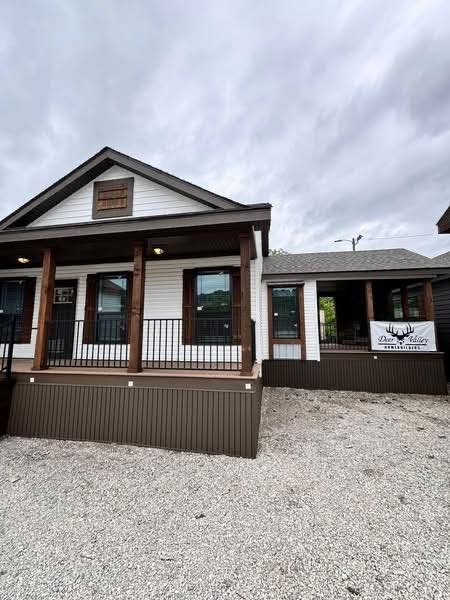 Alt text: "Small modern cabin with white siding and wood accents, featuring a front porch with black railings. Overcast sky sets a calm, serene mood."