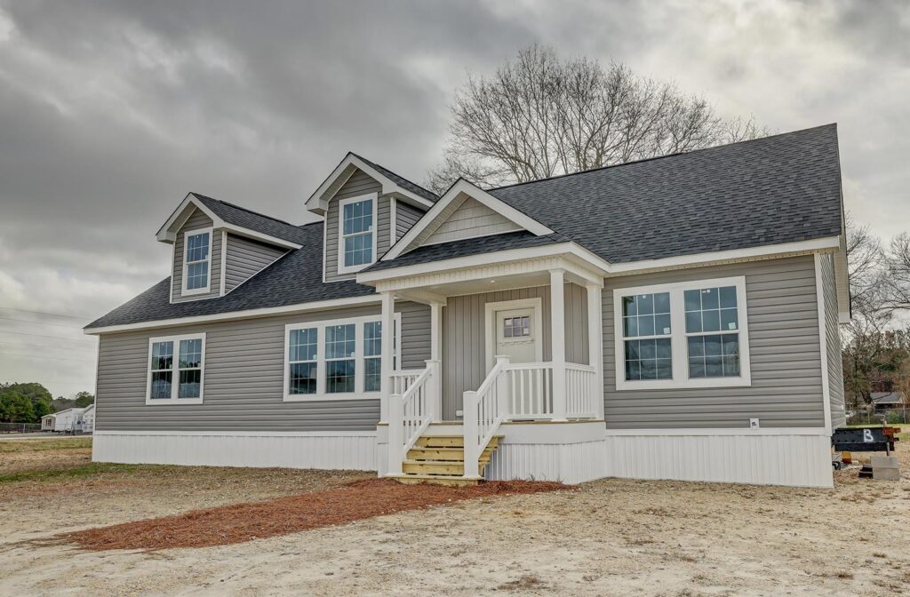 Single-story gray house with a black roof, white trim, and multiple windows. A small porch with steps is set against a cloudy sky, creating a calm mood.